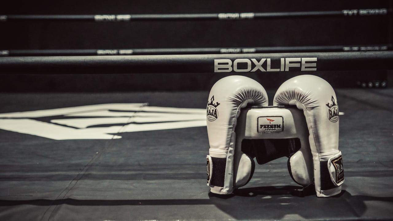 White boxing gloves resting on a boxing ring canvas with branding visible. Ideal for sports-themed content.