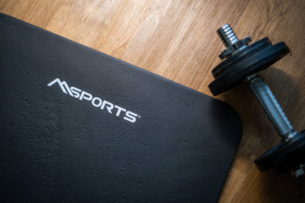 Flat lay of a gym mat and dumbbell on wooden floor, ideal for indoor workouts.