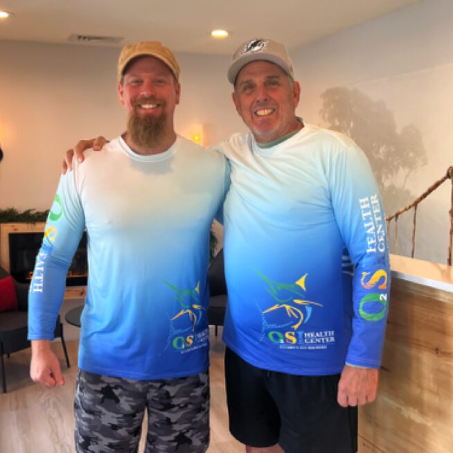 Two men in matching shirts smiling.